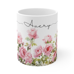 May include: White ceramic mug with a floral design featuring pink roses and green leaves. The mug has the name "Avery" written in black cursive on the front.
