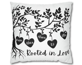 May include: A white cushion with a black silhouette of a tree with hearts hanging from the branches. The hearts have names written on them: Karen, Alexa, Alana, RJ, and Ellie. The text "Rooted in Love" is printed below the tree.