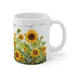 May include: White ceramic mug with a design of sunflowers in a field. The sunflowers are yellow with brown centers and green leaves. The mug has a black outline of a branch with leaves.
