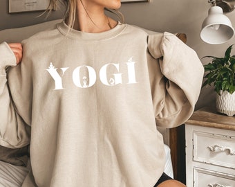 May include: A beige sweatshirt with the word "YOGI" printed in white on the front. The letters are stylized with yoga poses.