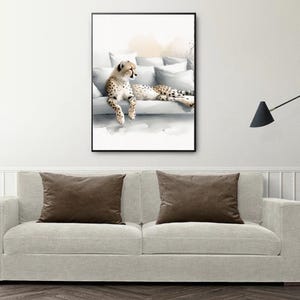 May include: A watercolor painting of a cheetah lying on a white couch with pillows. The cheetah is brown and black with spots. The painting is framed in a black frame.