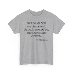 Op de afbeelding: Een lichtgrijs t-shirt met de quote "Hoe meer je alleen aan jezelf denkt, hoe kleiner je wereld wordt, en hoe ellendiger je wordt. - Cael Sanderson" in zwarte letters.