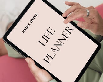 Puede incluir: Una tableta negra que muestra "LIFE PLANNER" en una fuente serif sobre un fondo rosa claro. El texto "FINORA STUDIO" está encima del texto principal. La tableta está sostenida por una persona con una blazer verde.