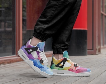 Peut inclure: Une paire de baskets blanches avec un motif aquarelle arc-en-ciel. Les baskets ont des accents noirs et une semelle intermédiaire blanche.