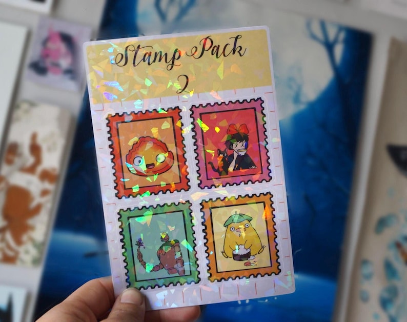 Puede incluir: Una hoja de pegatinas hologr&aacute;ficas con el texto "Stamp Pack 2" y cuatro sellos coloridos con personajes de la pel&iacute;cula animada "El castillo ambulante".