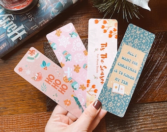 May include: Four Christmas-themed bookmarks with festive designs. The bookmarks feature illustrations of snowflakes, holly, ornaments, and a book with the text "Tis The Season" and "For More Books". One bookmark has the text "All I Want For Christmas Is To Finish My TBR" and another has the text "Ho Ho Ho".