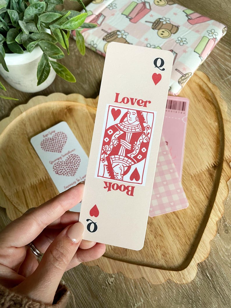 Peut inclure: Un marque-page rose avec un design de carte de jeu de la reine de c&oelig;ur rouge. La carte indique "Book Lover" et a un c&oelig;ur rouge dans le coin.