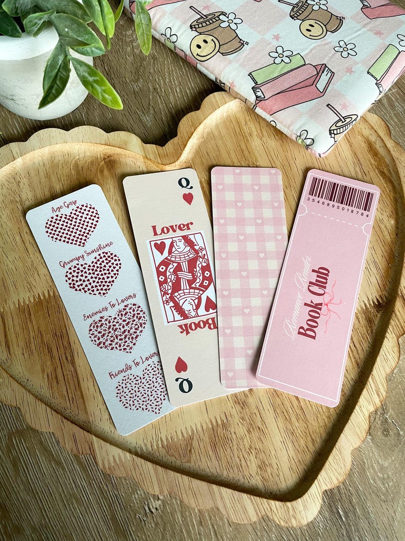 Peut inclure: Quatre marque-pages roses et rouges avec des motifs diff&eacute;rents. Un marque-page pr&eacute;sente un c&oelig;ur avec le texte "Age Gap", un autre marque-page pr&eacute;sente un c&oelig;ur avec le texte "Grumpy Sunshine", un autre marque-page pr&eacute;sente un c&oelig;ur avec le texte "Enemies To Lovers", et un autre marque-page pr&eacute;sente un c&oelig;ur avec le texte "Friends To Lovers". Le quatri&egrave;me marque-page pr&eacute;sente une carte de jeu de la reine de c&oelig;ur avec le texte "Lover" et "Book". Le dernier marque-page est rose avec du vichy blanc et le texte "Romance Reader Book Club".