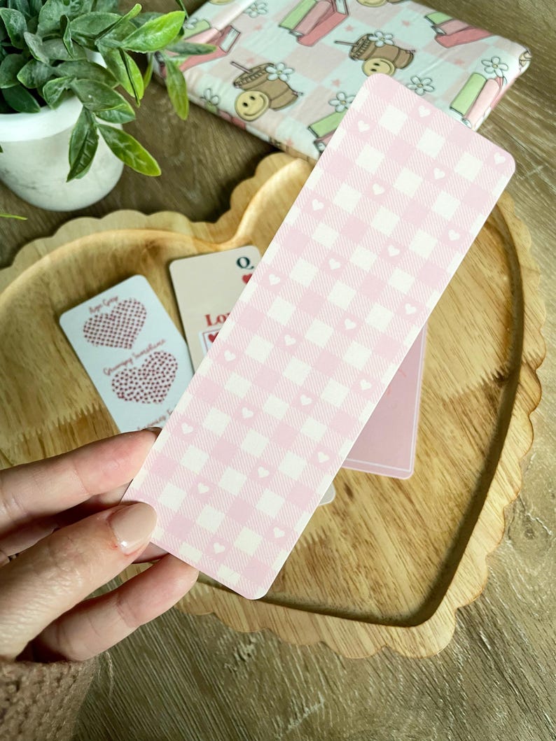 Peut inclure: Un marque-page en gingham rose et blanc avec de petits c&oelig;urs blancs. Le marque-page est fait de carton &eacute;pais et a une surface l&eacute;g&egrave;rement textur&eacute;e.