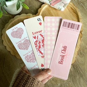 Peut inclure: Quatre marque-pages roses avec des motifs diff&eacute;rents. Un marque-page pr&eacute;sente une carte &agrave; jouer avec la reine de c&oelig;ur et le mot "Lover". Un autre marque-page a un motif vichy rose et blanc. Un troisi&egrave;me marque-page a un motif de c&oelig;ur rose et blanc avec le texte "Age Gap, Grumpy Sunshine, Enemies to Love, Friends to". Le quatri&egrave;me marque-page est rose avec le texte "Romance Reader Book Club" et un code-barres avec le num&eacute;ro "3546895018784".
