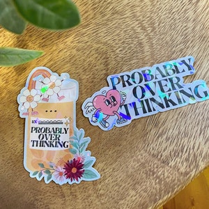May include: Two holographic stickers with the text "Probably Overthinking" in black lettering. One sticker features a cartoon heart with wings and the other sticker features a cartoon pill bottle with flowers.