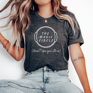 May include: A dark gray t-shirt with a white circle graphic that says "The Magic Circle (doesn't like you either)".