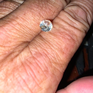 Puede incluir: Una piedra preciosa redonda y transparente con facetas, sostenida en una mano.