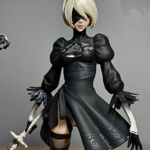 Könnte beinhalten: Detaillierte Figur einer Figur mit kurzen blonden Haaren, einer schwarzen Augenbinde und einem schwarzen Kleid. Die Figur hält ein silbernes Schwert. Das Kleid hat dekorative Muster und die Figur trägt schwarze Handschuhe und Stiefel. Sammlerstück.