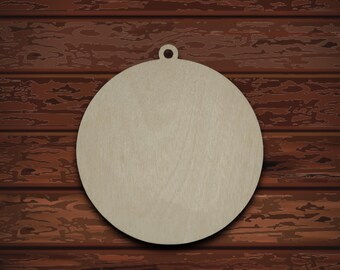 May include: A round, unfinished wooden ornament with a small hole at the top for hanging. The ornament is set against a dark brown wood background, with pine needles and pine cones at the bottom. The text "Yarn, Wood and More" is visible.