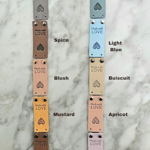 May include: Ten leather labels with different colors and the text "Made with LOVE" in black. The colors are grey, blue, spice, light blue, blush, buiscuit, mustard, apricot, chocolate, and lavender.