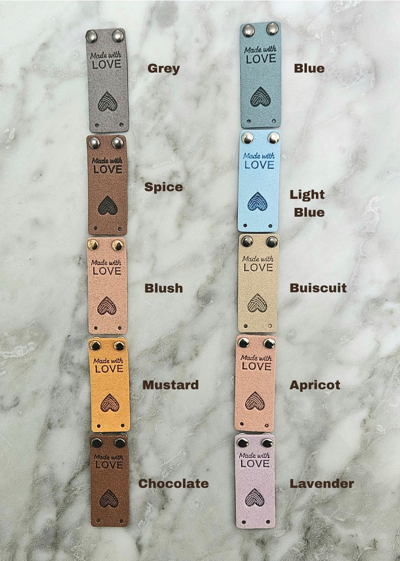 May include: Ten leather labels with different colors and the text "Made with LOVE" in black. The colors are grey, blue, spice, light blue, blush, buiscuit, mustard, apricot, chocolate, and lavender.