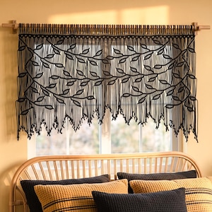May include: A black macrame window valance featuring a detailed leaf pattern created with intricate knotted cord work. The valance hangs from a wooden rod and displays a series of vertical fringe strands that form a pointed, uneven bottom edge.