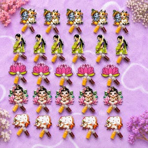May include: A collection of twenty-five acrylic charms arranged in five rows. The charms feature illustrations of Krishna with a cow, a pregnant person in a green sari, pink lotus flowers, baby Krishna on a lotus, and a cow, each with two small vials.