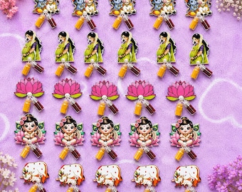 May include: A collection of twenty-five acrylic charms arranged in five rows. The charms feature illustrations of Hindu deities, lotus flowers, and cows, each attached to two small glass vials filled with yellow and red colored powders.