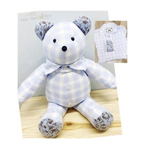 May include: A handmade teddy bear wearing a light blue and white plaid shirt. The bear has blue floral patterned ears and paw pads. A smaller image of a matching shirt is in the upper right corner. The bear is sitting on a wooden surface.