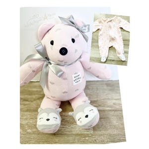 May include: A pink teddy bear with a silver bow and accents, wearing gray and white fox-shaped slippers. The bear has a tag that says "Mummy Adores". A pink baby onesie with white polka dots is also shown.