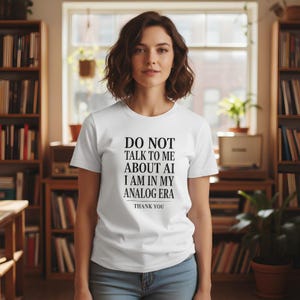 May include: A white short-sleeved t-shirt featuring black text that reads: DO NOT TALK TO ME ABOUT AI I AM IN MY ANALOG ERA THANK YOU. The shirt has a crew neckline and a standard fit, made of a plain fabric with a clear, centered graphic print.