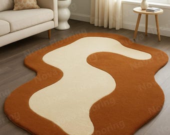 May include: A brown and cream-colored, abstract-shaped rug. The rug has a wavy, organic design with a cream-colored center and a brown border. The rug is placed on a wooden floor in a living room setting.