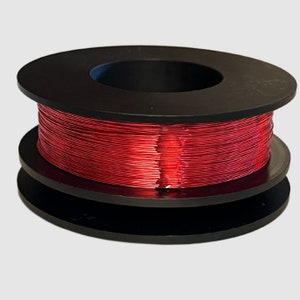 May include: A black plastic spool holds a tightly wound coil of red wire. The wire is a vibrant red colour and appears to be metallic. The spool has a circular design with a central opening. The background is a plain, light grey.