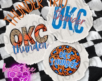 Peut inclure: Trois motifs circulaires avec des graphiques OKC Thunder. L'un présente un ballon de basket avec un imprimé léopard, un autre a OKC avec un ballon de basket, et le troisième a OKC Thunder en bleu. Les mots "Thunder Trio" sont en haut.