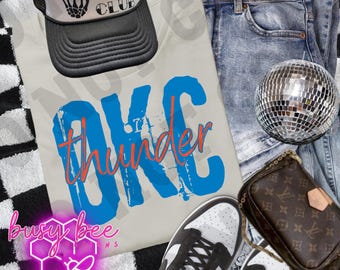 May include: A casual fashion ensemble featuring a light gray t-shirt with "OKC Thunder" in blue and orange, a black and white trucker hat, blue jeans, and black and white sneakers. A small disco ball and a brown purse complete the look.