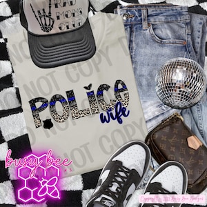 Peut inclure: Un t-shirt crème avec l'inscription "Police Wife" en noir, bleu et imprimé léopard. Une casquette de camionneur noire et blanche avec "Rad Moms Club" est posée dessus. L'image comprend un jean, des baskets et une boule disco.