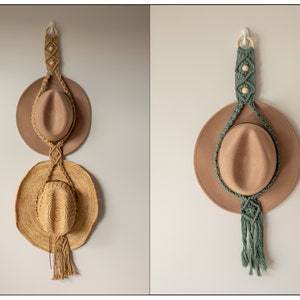 May include: Two hats hanging on a wall using a macrame hat holder. The top hat is brown felt and the bottom hat is a straw cowboy hat. The macrame holder is made with natural coloured cord and has wooden beads.