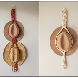 May include: Two macrame hat holders with wooden rings at the top. One is red and the other is cream. Both are hanging on white walls with hats on them.