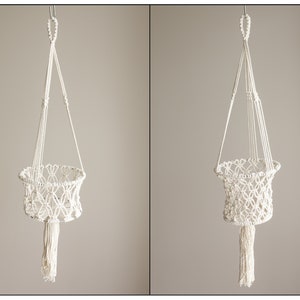 May include: A white macrame hanging planter with a tassel. The planter is made of cotton cord and has a round shape. It is perfect for hanging plants or other small items.