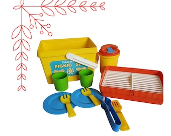 Puede incluir: Un juego de picnic de plástico amarillo con una nevera, dos vasos, dos platos, una parrilla, un juego de pinzas y una jarra. La nevera tiene las palabras "Fisher Price Picnic Set" impresas.
