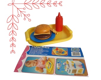 Puede incluir: Una bandeja de plástico amarilla con una hamburguesa de juguete, una botella de ketchup y papas fritas. La bandeja está etiquetada con "Fisher-Price" y tiene el texto "Cheeseburger & Chips" en inglés, alemán, español, italiano y portugués. La bandeja es parte de un juego de cocina de juguete.
