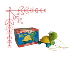 May include: A green and yellow toy turtle with a blue sailor hat pulls a yellow rope. The box reads "Tag-Along Turtle" and "Fisher-Price".
