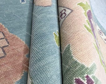 May include: Close-up of a rolled-up rug with a colorful floral pattern. The rug has a light blue background with pink, green, and purple flowers.