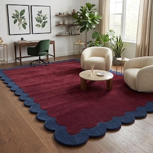 May include: A large rectangular area rug featuring a deep burgundy center and a thick, scalloped navy blue border. The rug has a textured, plush pile surface and is positioned on a light brown wooden floor in a room with furniture.