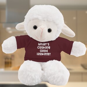 May include: White plush lamb wearing a maroon shirt with the text "What's cooking good looking?" printed in white.