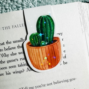 May include: A sticker of two green cacti in a brown pot with a glittery background. The cacti are in a cartoon style and have a white outline.