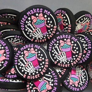 Peut inclure: Gros plan sur plusieurs boutons ronds noirs avec un motif rose, blanc et violet. Les boutons représentent une main squelettique tenant une tasse de café avec un nœud rose sur le dessus. Le texte sur les boutons indique "Coffee makes me a nicer person".