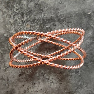 Könnte beinhalten: Ein Armband aus Kupferdraht mit geflochtenem Design. Das Armband besteht aus mehreren Drähten, die miteinander verdreht sind, um ein einzigartiges und komplexes Muster zu schaffen.