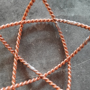 May include: Close-up of a copper wire star-shaped frame. The wire is twisted and has a shiny, metallic finish.