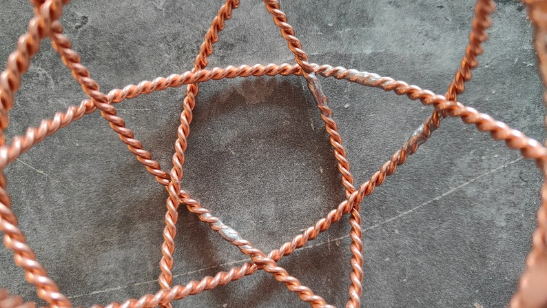 May include: Close-up of a copper wire star-shaped frame. The wire is twisted and has a shiny, metallic finish.