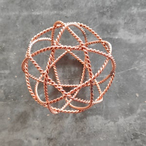 May include: A copper wire sphere sculpture with a geometric design. The sphere is made of multiple intertwined wires, creating a complex and intricate pattern.