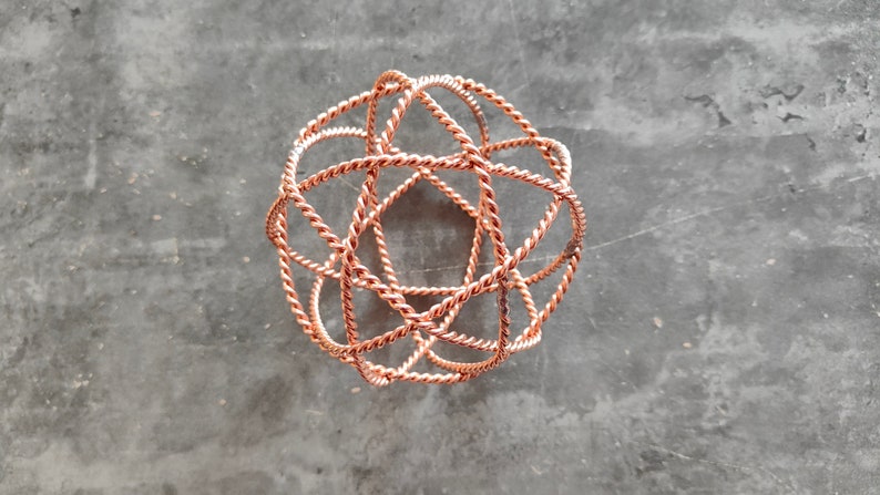 May include: A copper wire sphere sculpture with a geometric design. The sphere is made of multiple intertwined wires, creating a complex and intricate pattern.