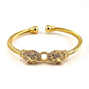 May include: A gold bangle bracelet with a twisted design and two animal head charms. The charms are covered in clear rhinestones.