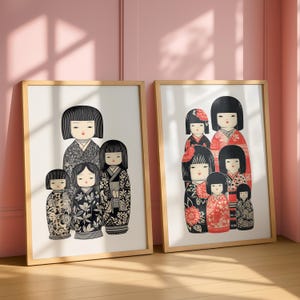 Puede incluir: Dos impresiones enmarcadas con mu&ntilde;ecas Kokeshi japonesas. Las mu&ntilde;ecas est&aacute;n representadas con atuendos tradicionales con patrones florales y geom&eacute;tricos en negro, blanco y rojo. Las impresiones se exhiben contra una pared rosa y un suelo de madera.